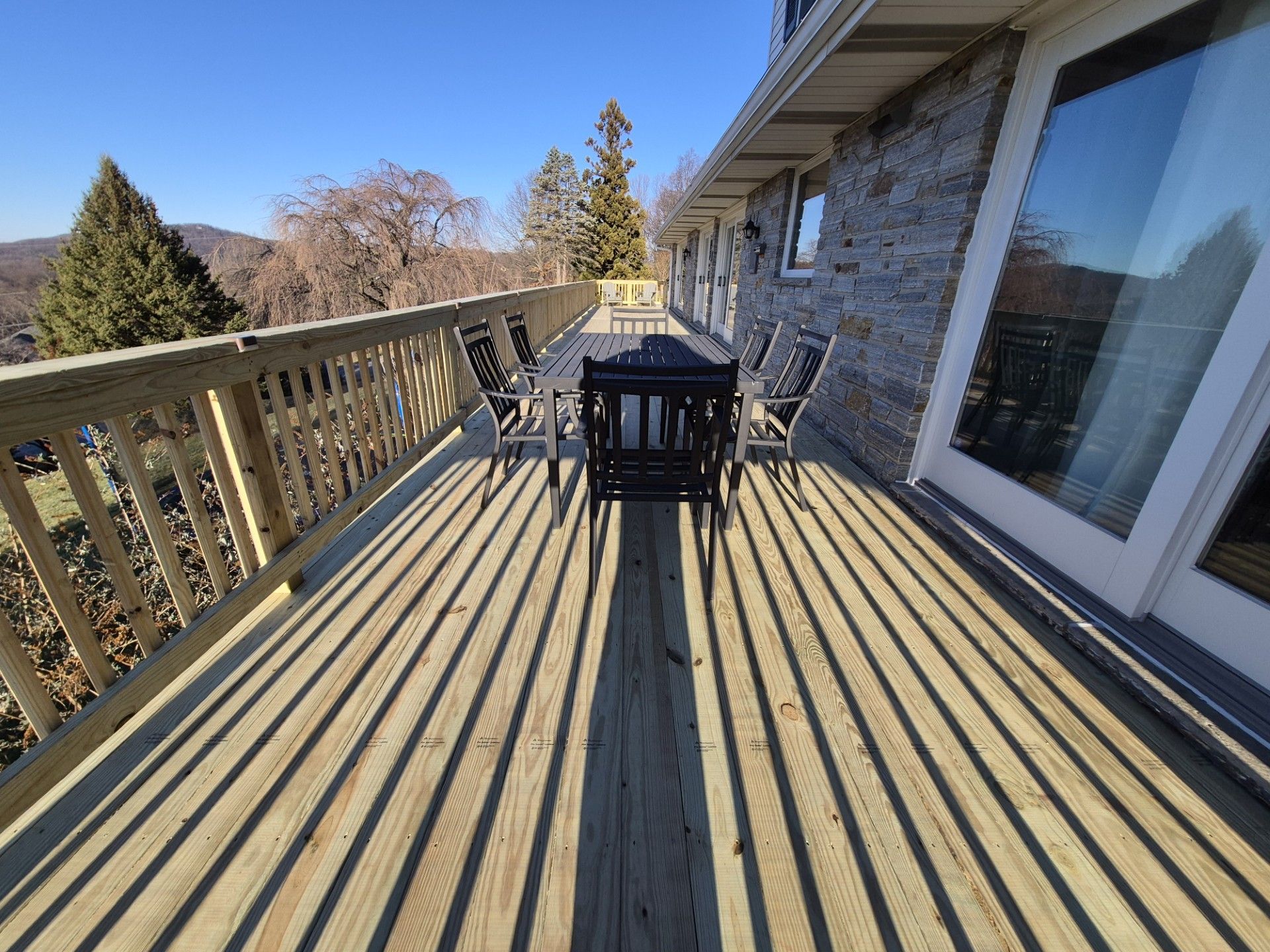 Wooden deck with outdoor furniture next to a house, sunny day, shadows.