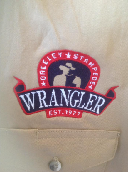 A wrangler logo is embroidered on a tan shirt
