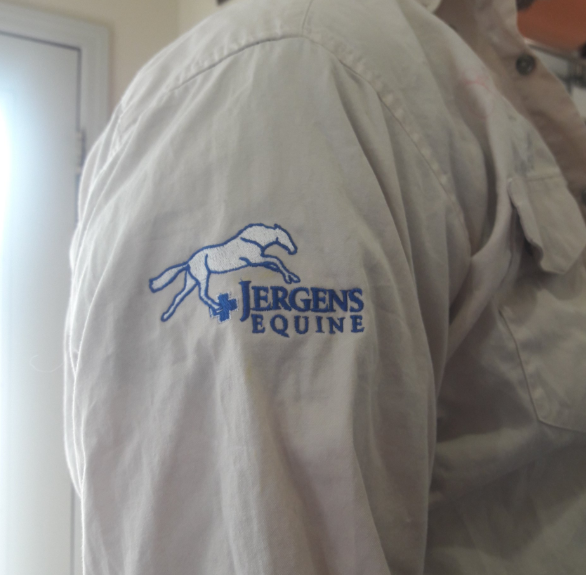 A person is wearing a white shirt with the jergens equine logo on the sleeve