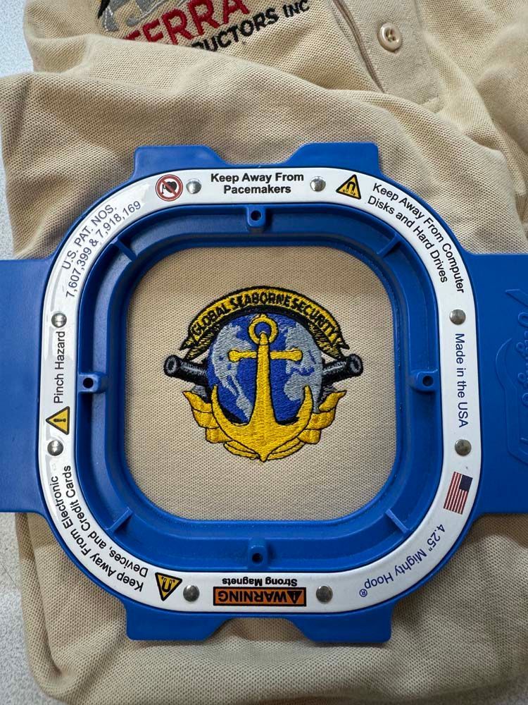 Embroidered patch of anchor inside embroidery hoop, on tan fabric.