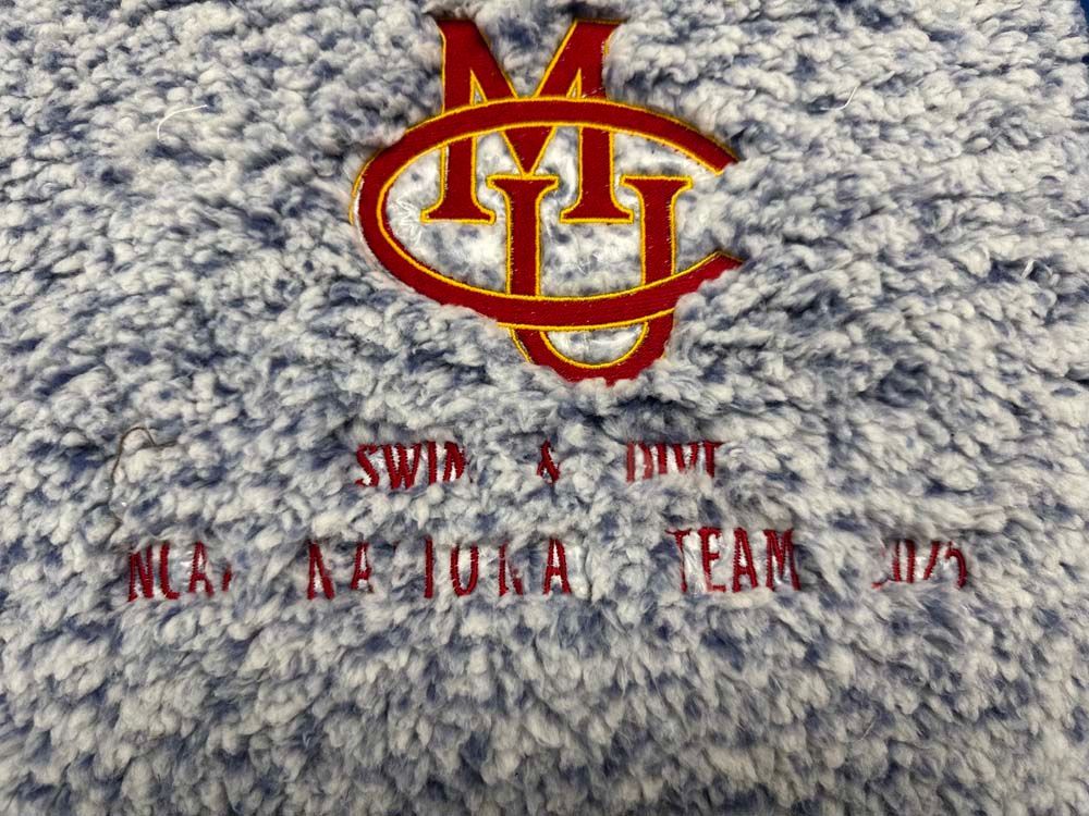 Embroidered maroon MJC logo on fuzzy fabric.