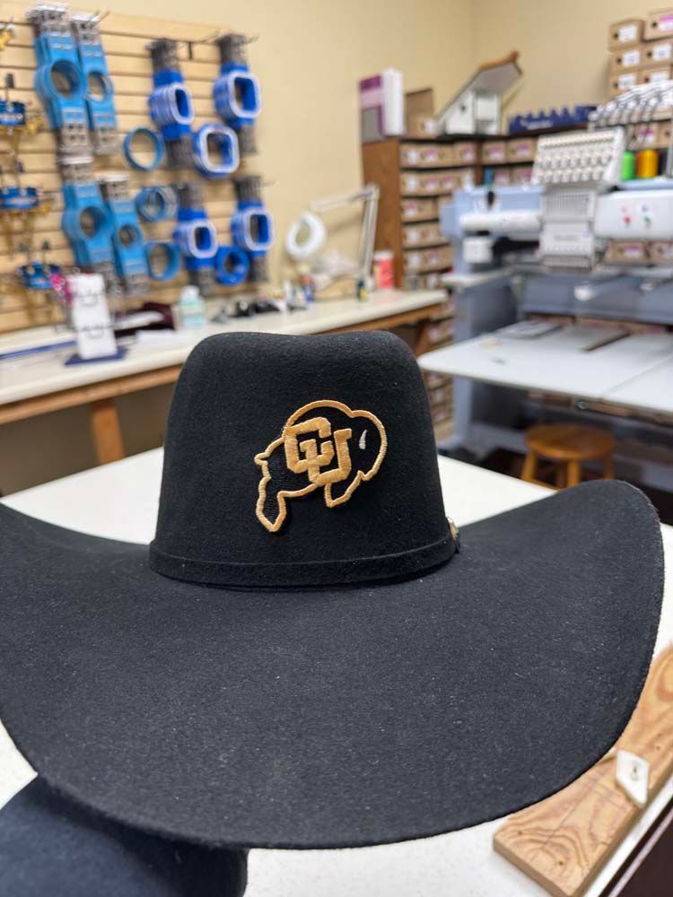 Black cowboy hat with a CU logo in a workshop setting.