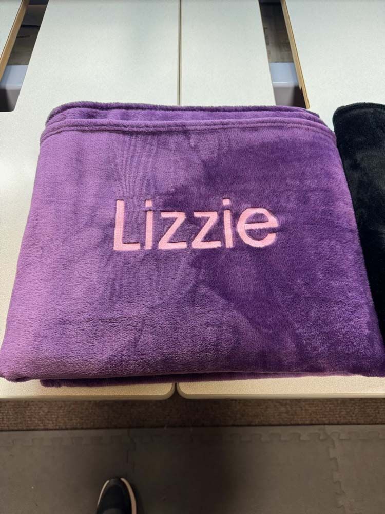 Purple blanket, folded, with text embroidered in pink.