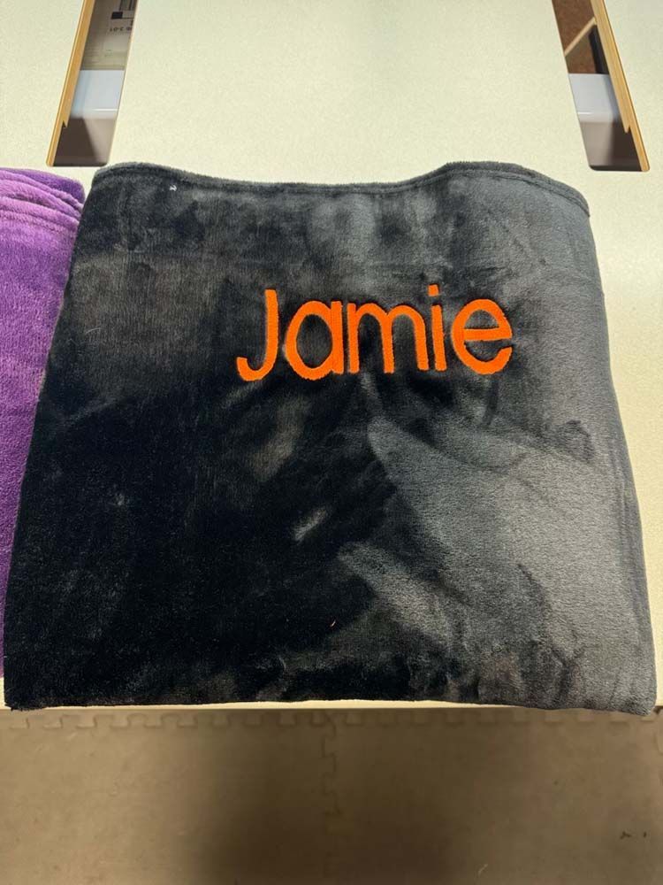 Black blanket with orange text embroidery.