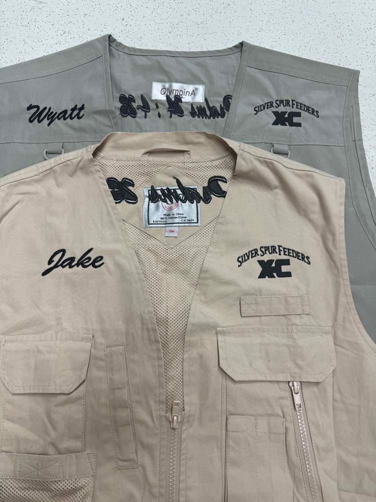 Two tan and gray vests with pockets and zippers.