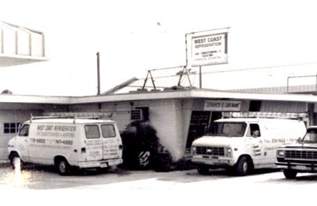 Two white vans parked outside a small storefront with a sign above the entrance.