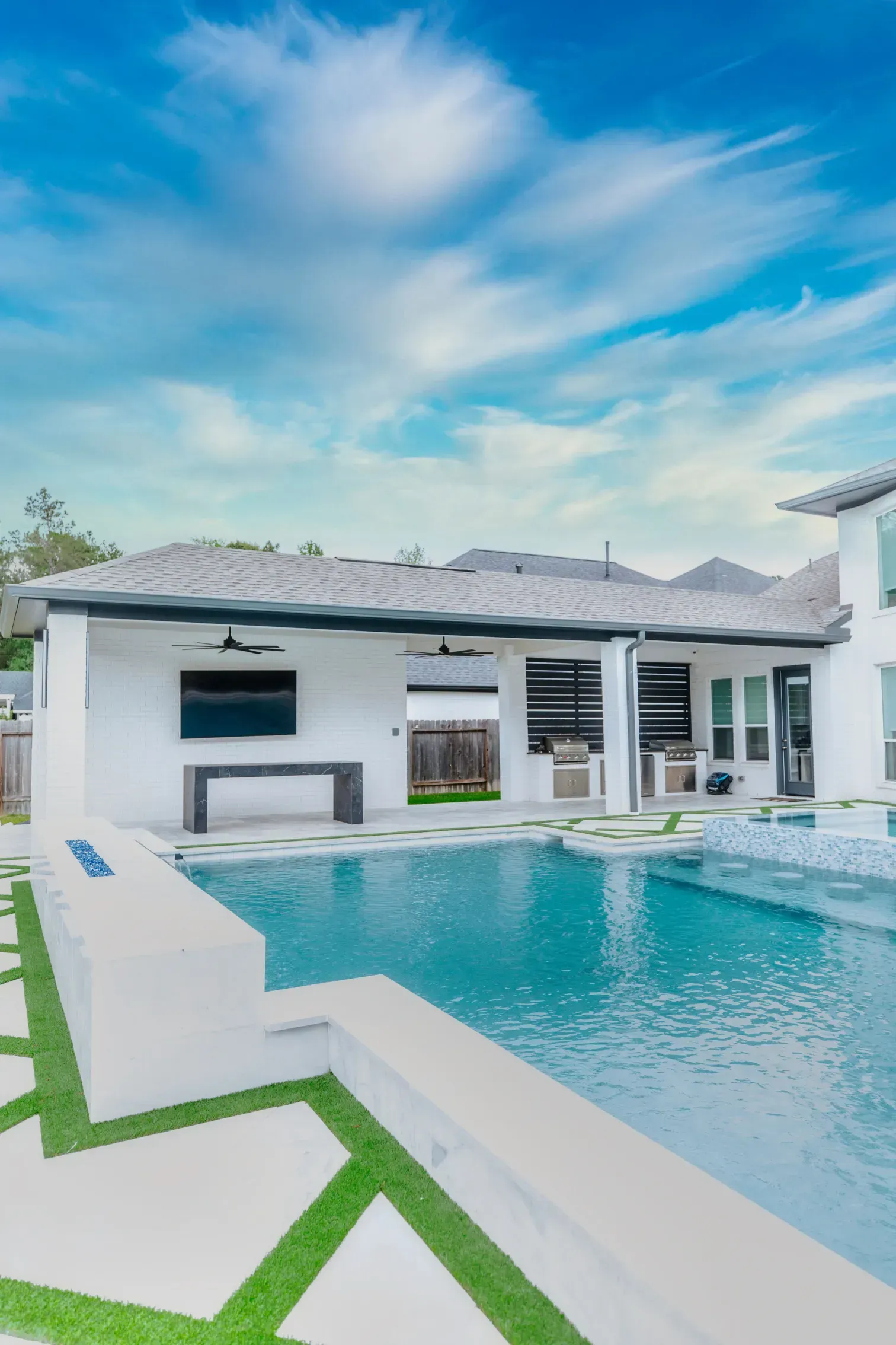 Modern white house with a turquoise pool and blue sky over a tiled patio