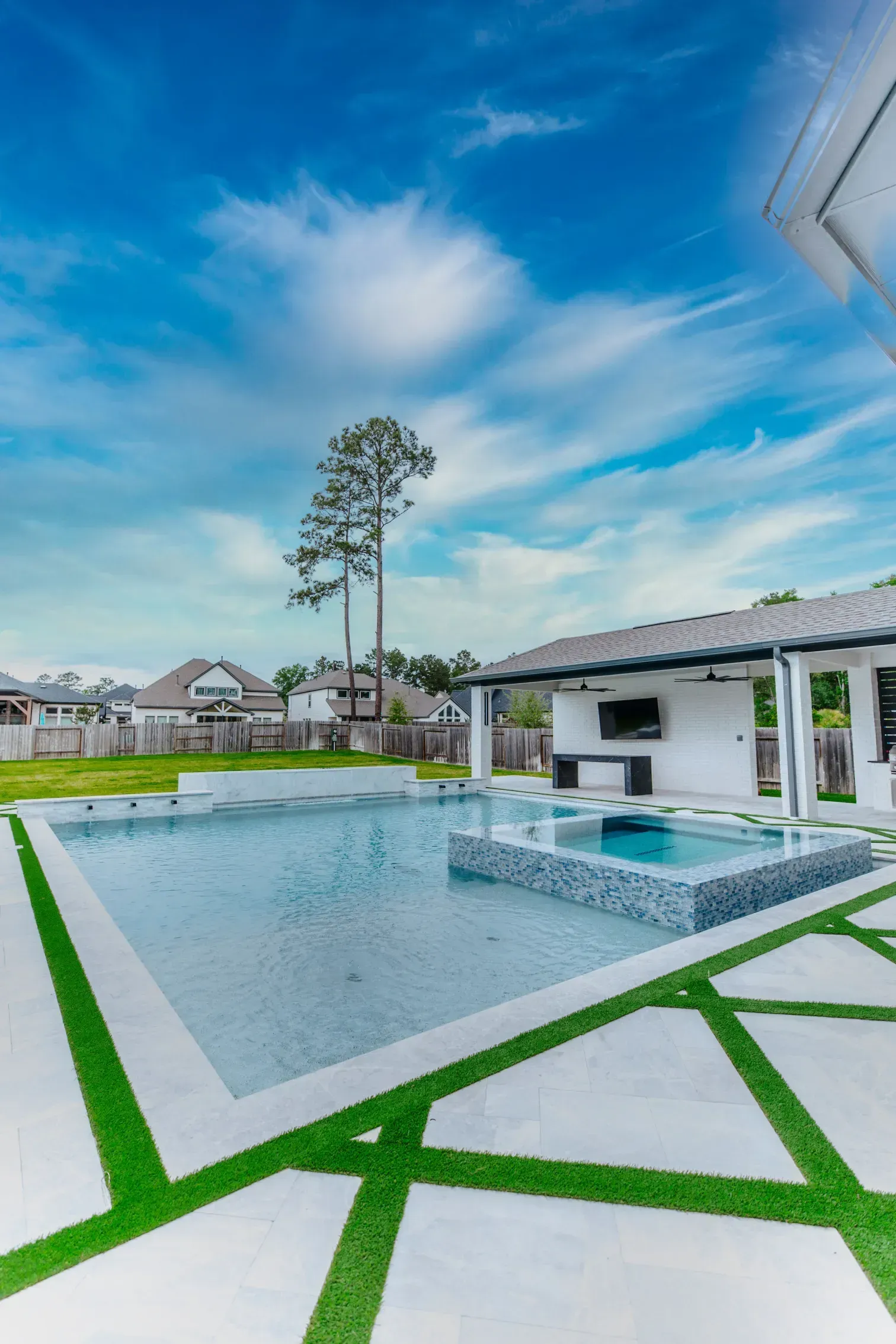 Modern backyard pool with white pavilion, geometric lawn, and a tall tree under a blue sky