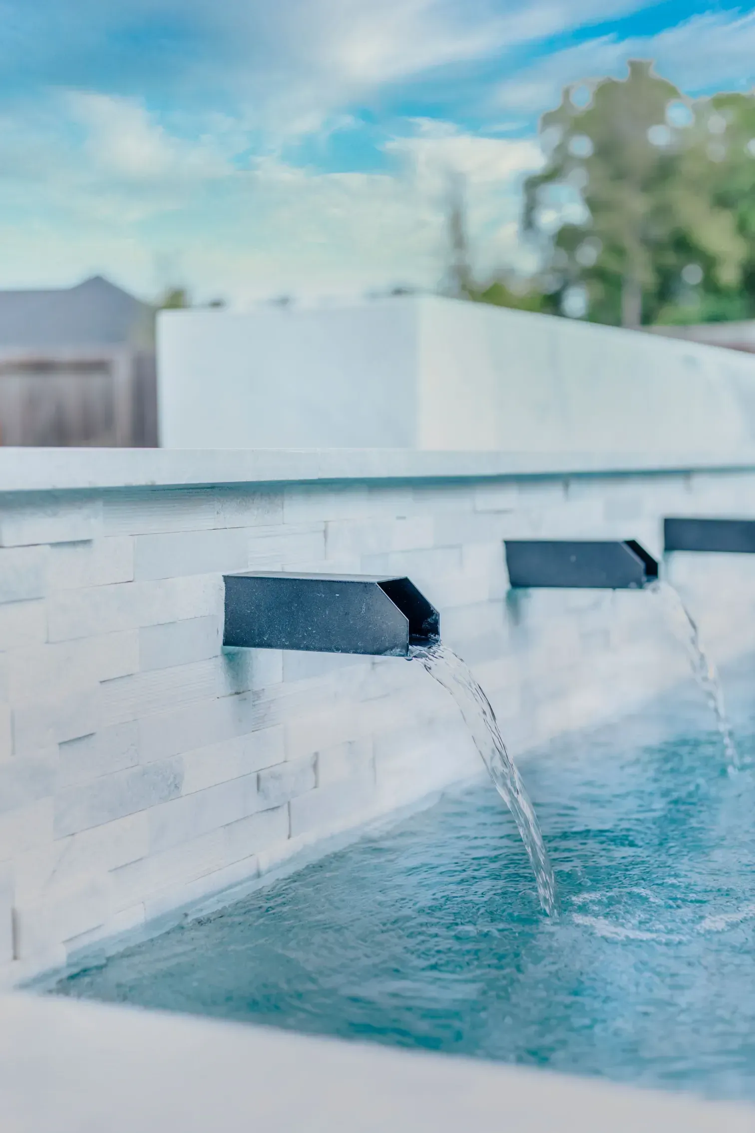 Modern white wall fountain with water flowing into a blue pool under a bright sky