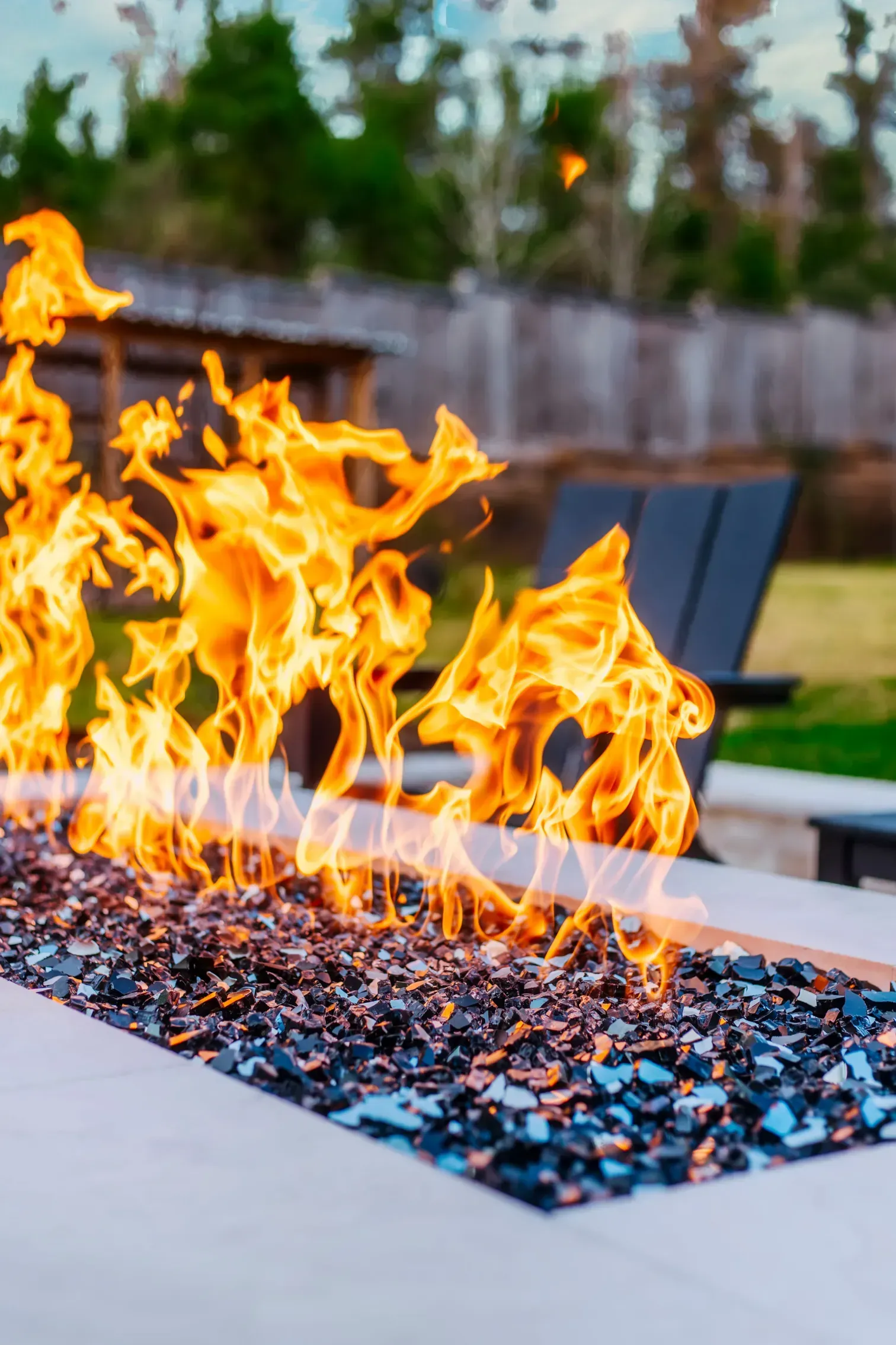 Modern gas fire pit with bright flames and blue lounge chairs outdoors
