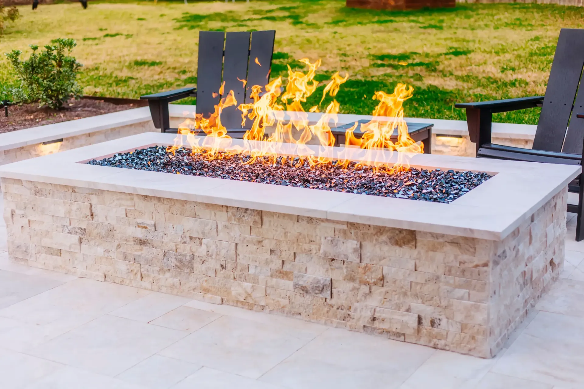 Modern stone fire pit burning outdoors on a patio with grass in the background