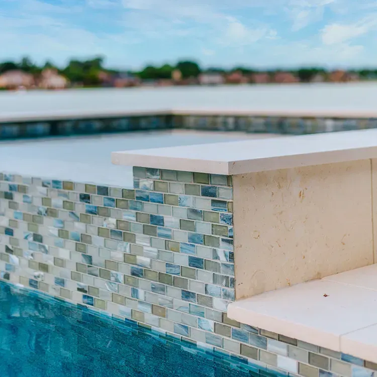 Poolside mosaic-tiled bench with turquoise water and a blurred waterfront background