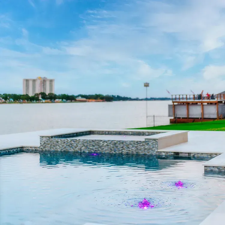 Rooftop infinity pool with blue water, stone ledge, and distant city skyline under a clear sky