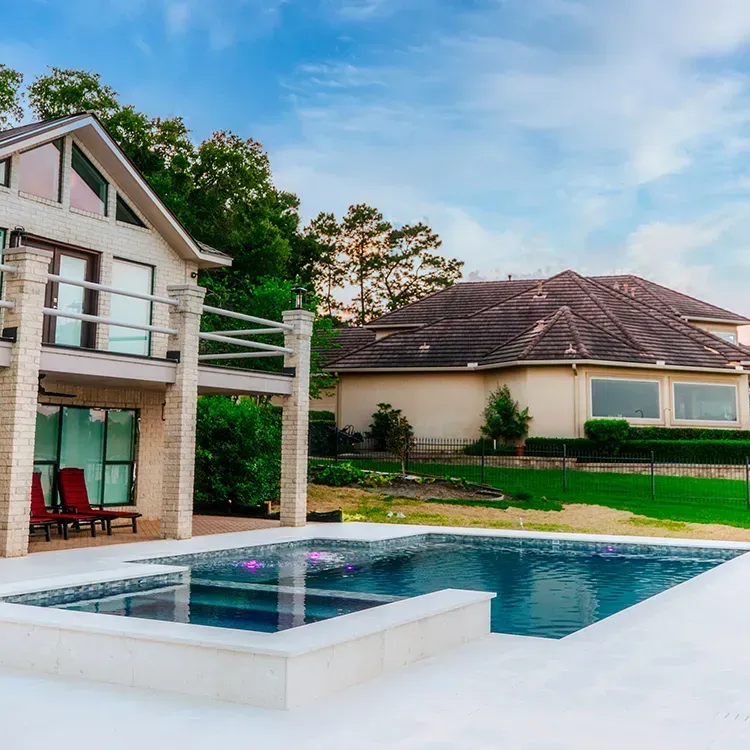 Modern backyard with a house, patio, and blue swimming pool under a partly cloudy sky