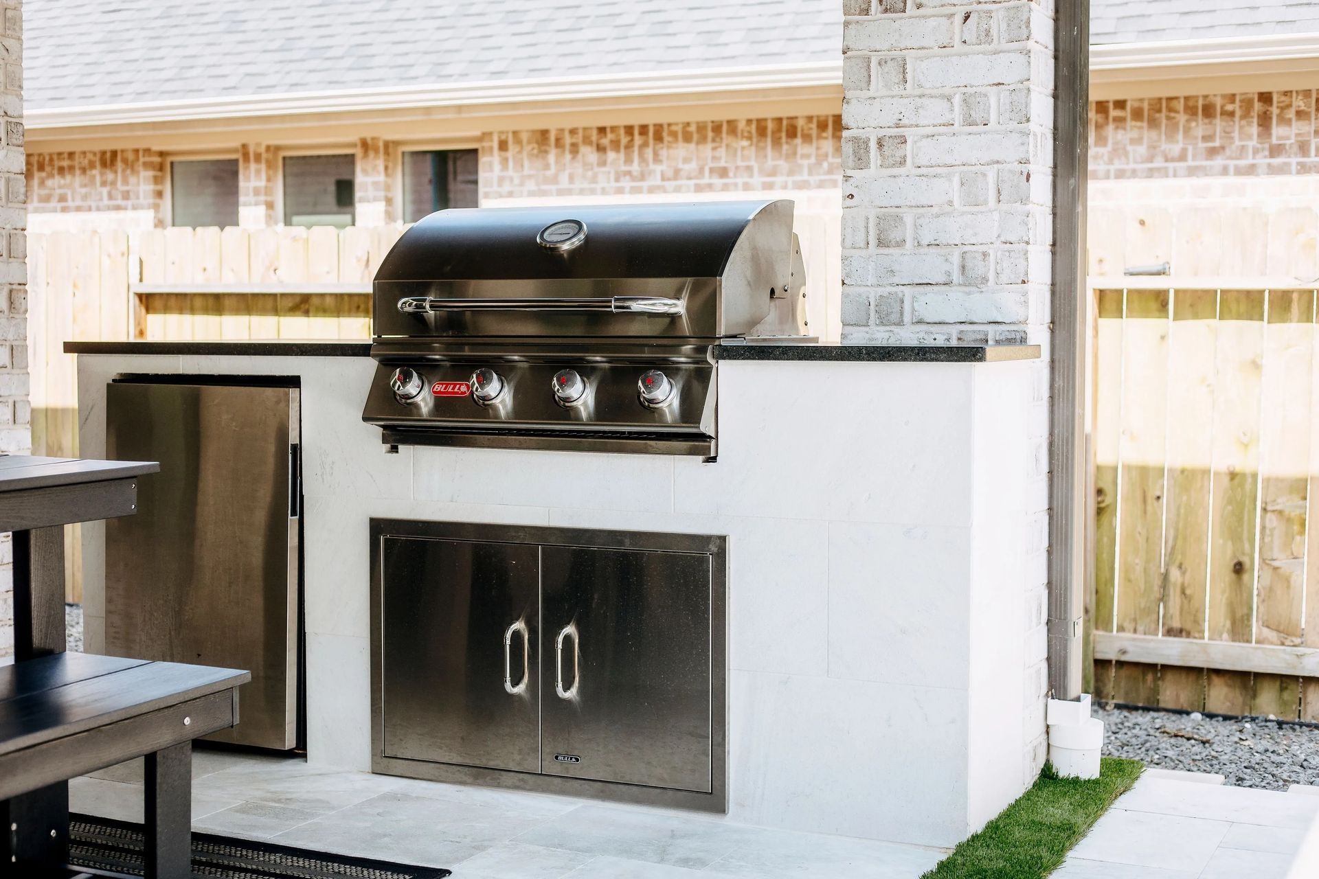 Outdoor built-in stainless steel grill with white stone surround in a backyard patio