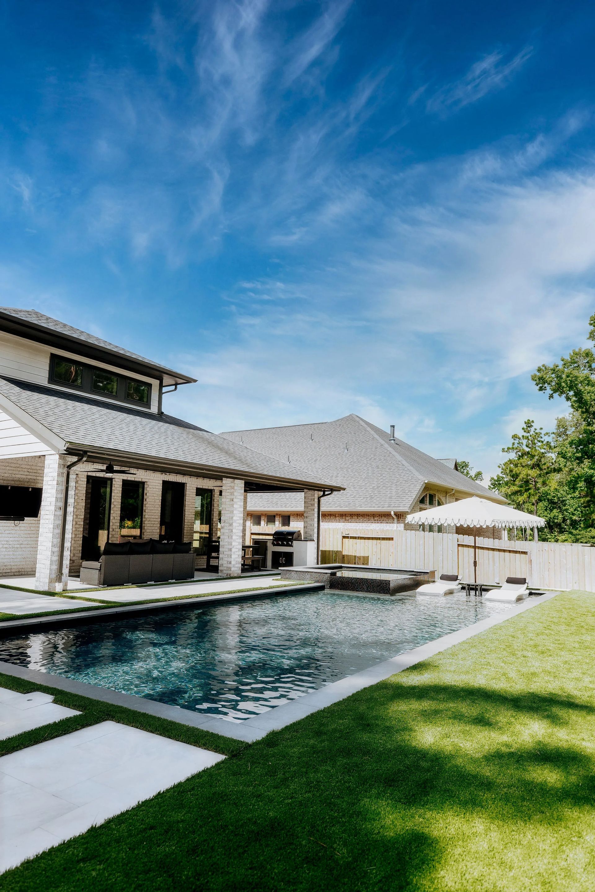 Modern house with a backyard pool, green lawn, and patio under a blue sky