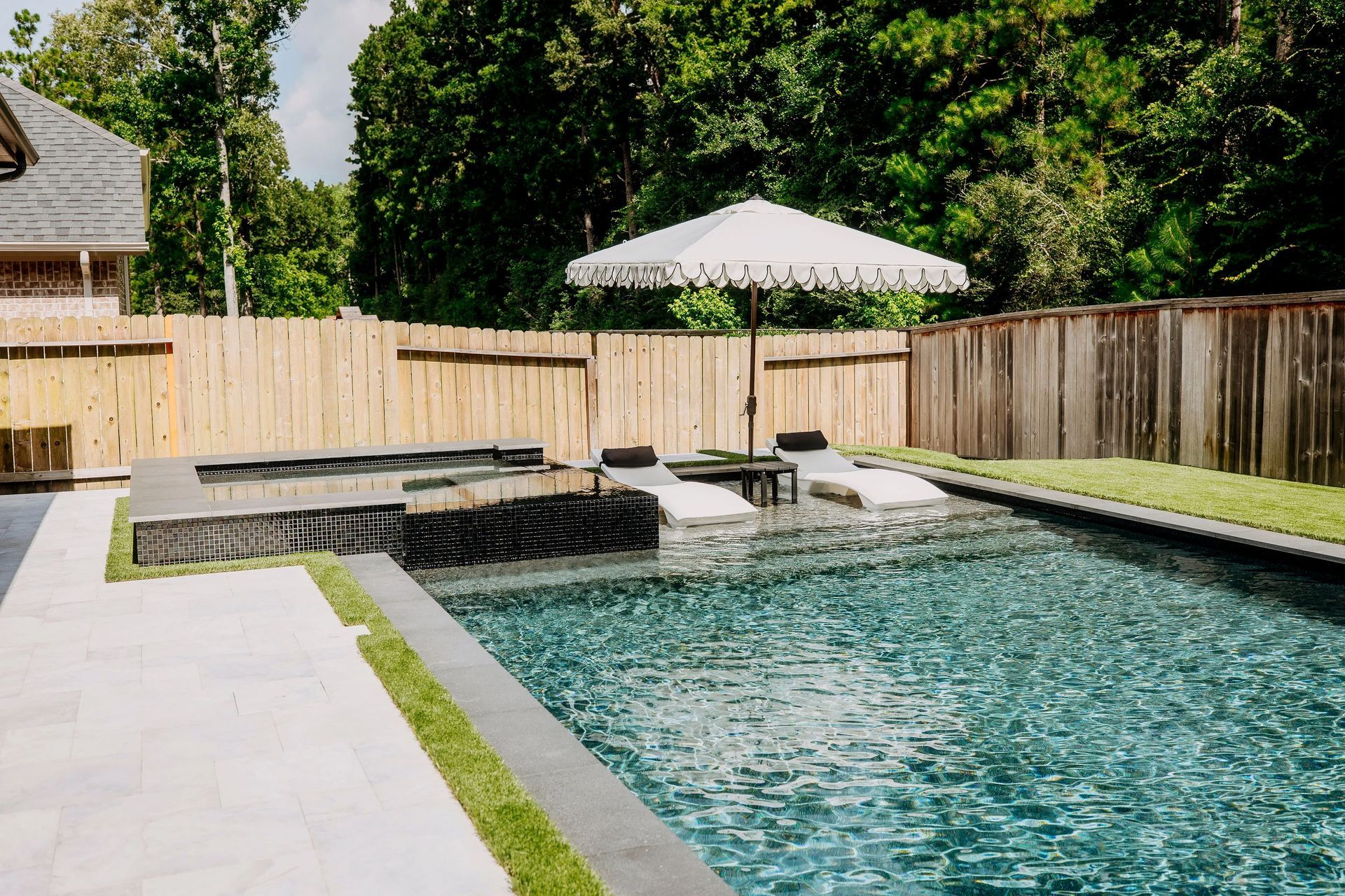 Backyard pool with stone coping, umbrella, lounge chairs, and wooden privacy fence