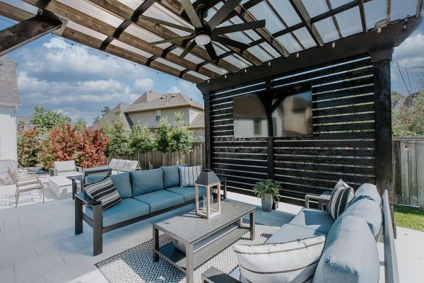Covered patio with blue outdoor seating, coffee table, and black slatted wall under a pergola
