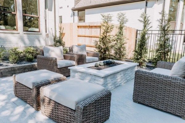 Wicker patio seating around a low white fire pit on a sunlit stone terrace.