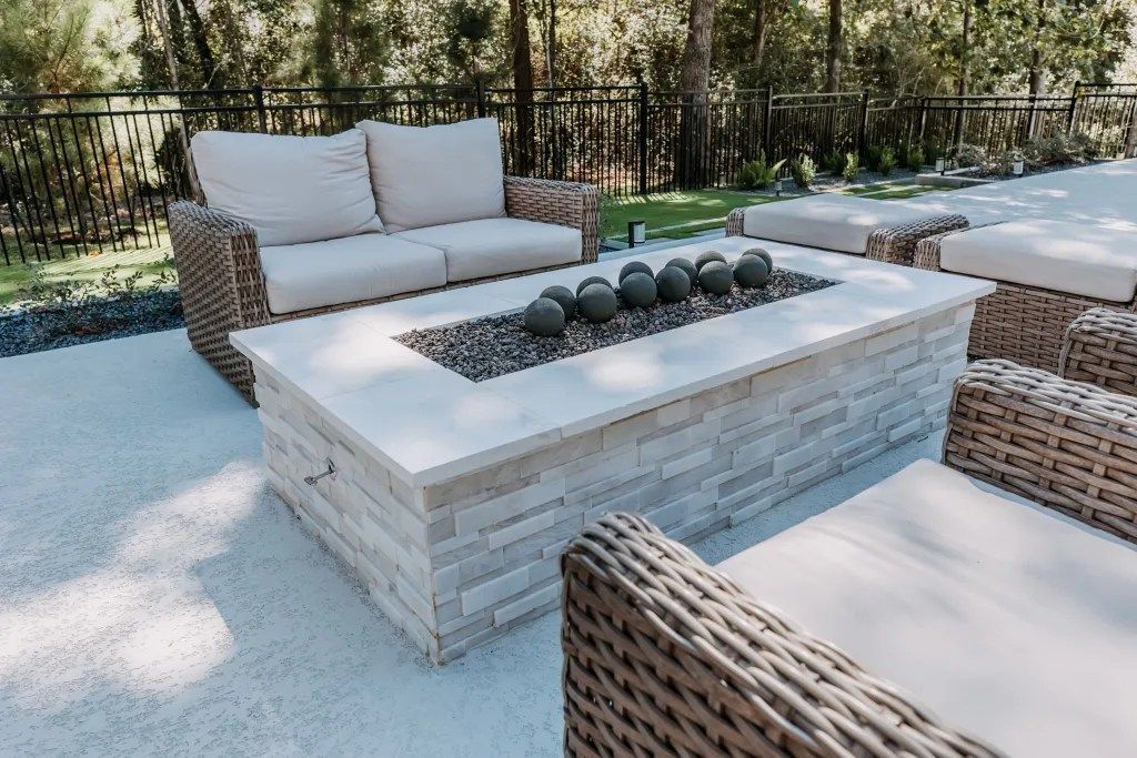 Outdoor patio with wicker furniture and a low white coffee table, set on a light gravel surface.