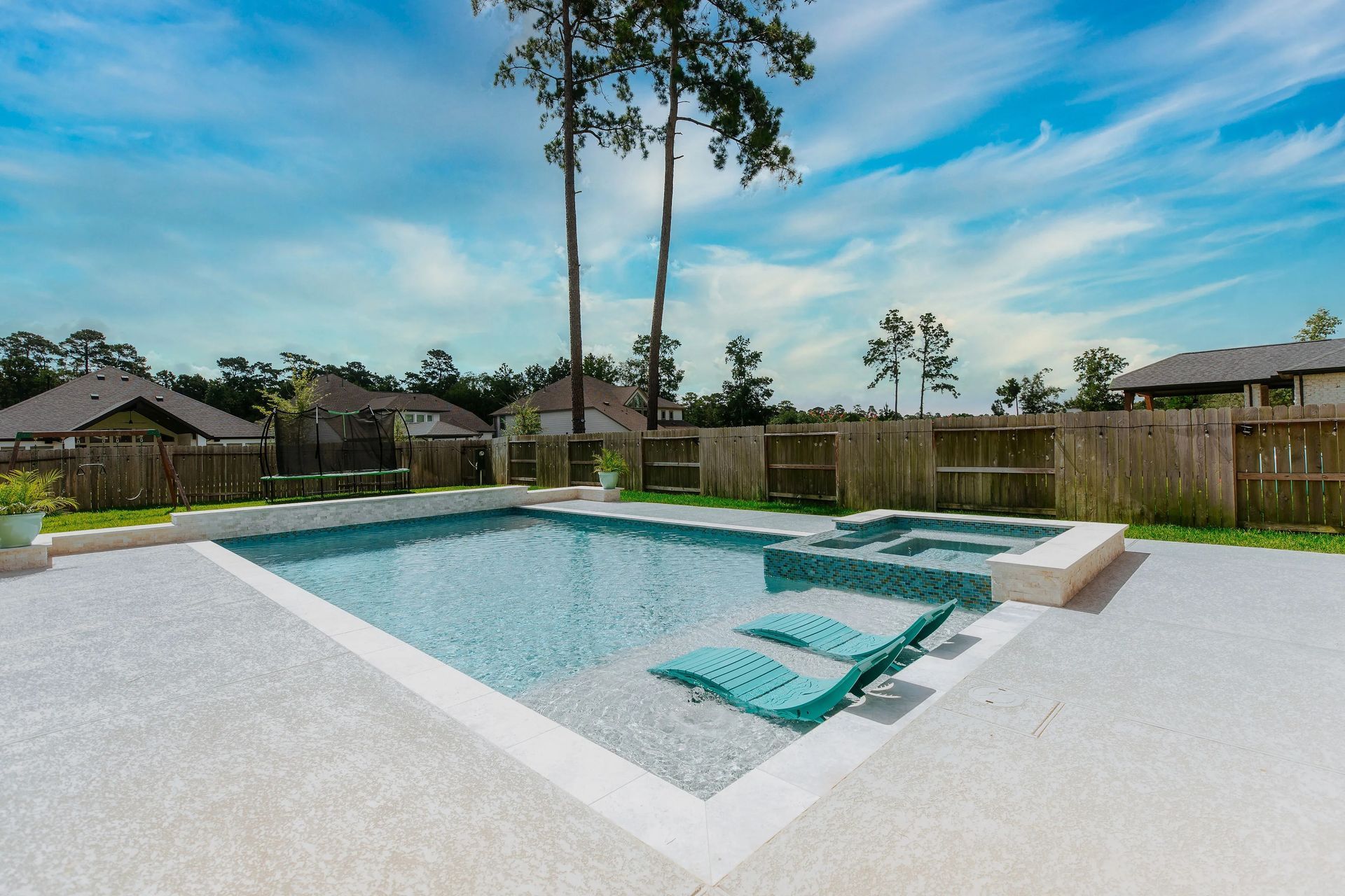 Backyard swimming pool with a shallow tanning ledge, surrounded by a concrete patio and wooden fence