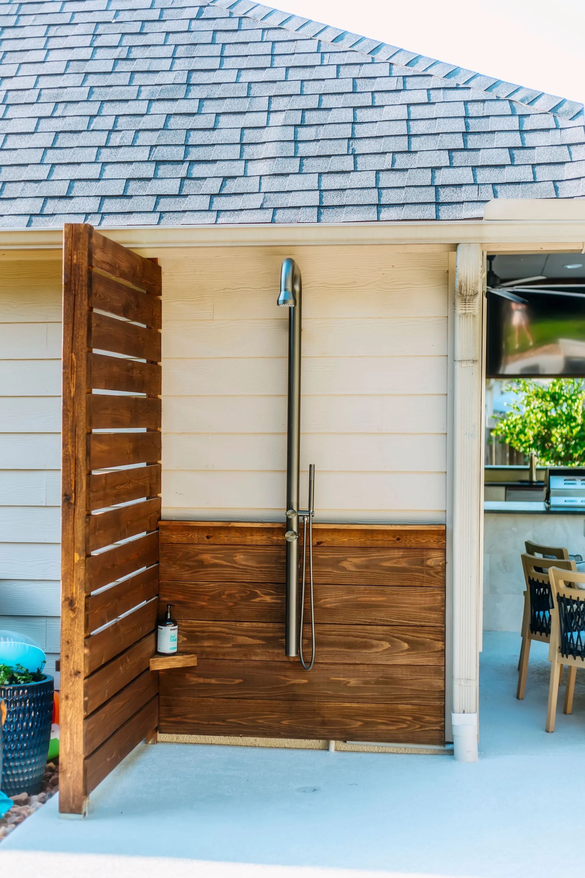 Outdoor shower area with wood privacy panels and a mounted shower fixture under a shingled roof