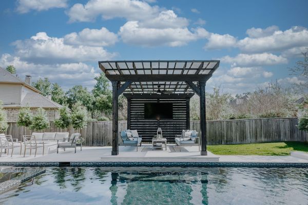 Backyard pool with a covered patio, lounge chairs, and a cloudy sky отражение in the water