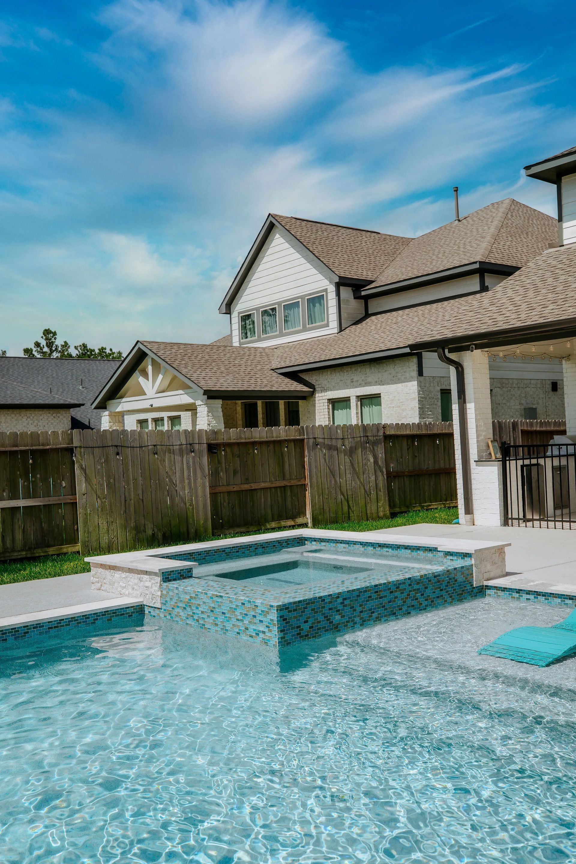 Backyard pool with turquoise water beside a house under a blue sky