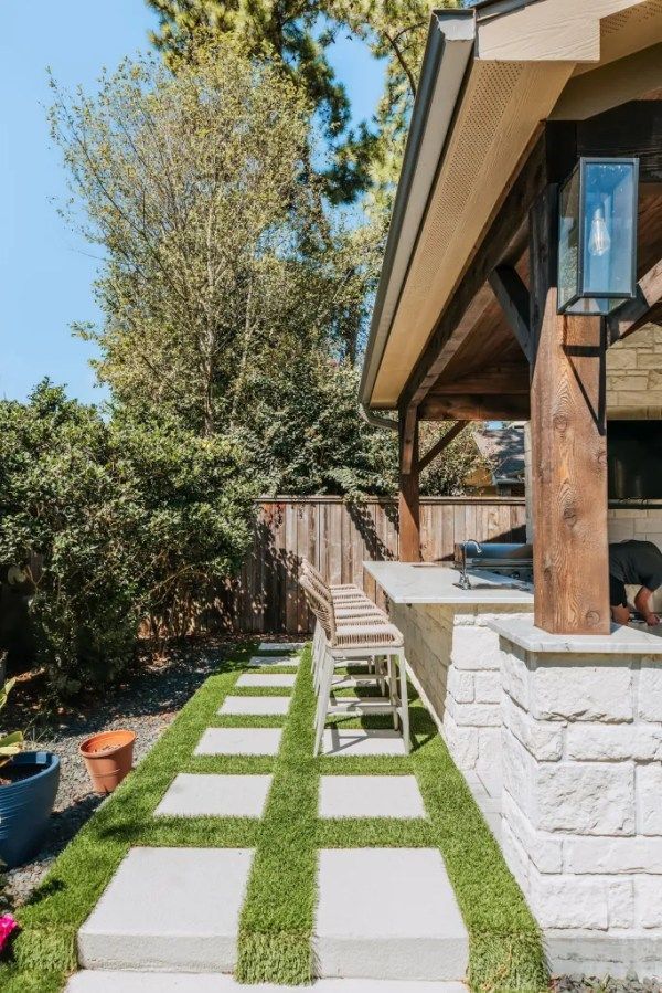 Backyard patio walkway with square stepping stones and grass between, beside a house and wooden fence