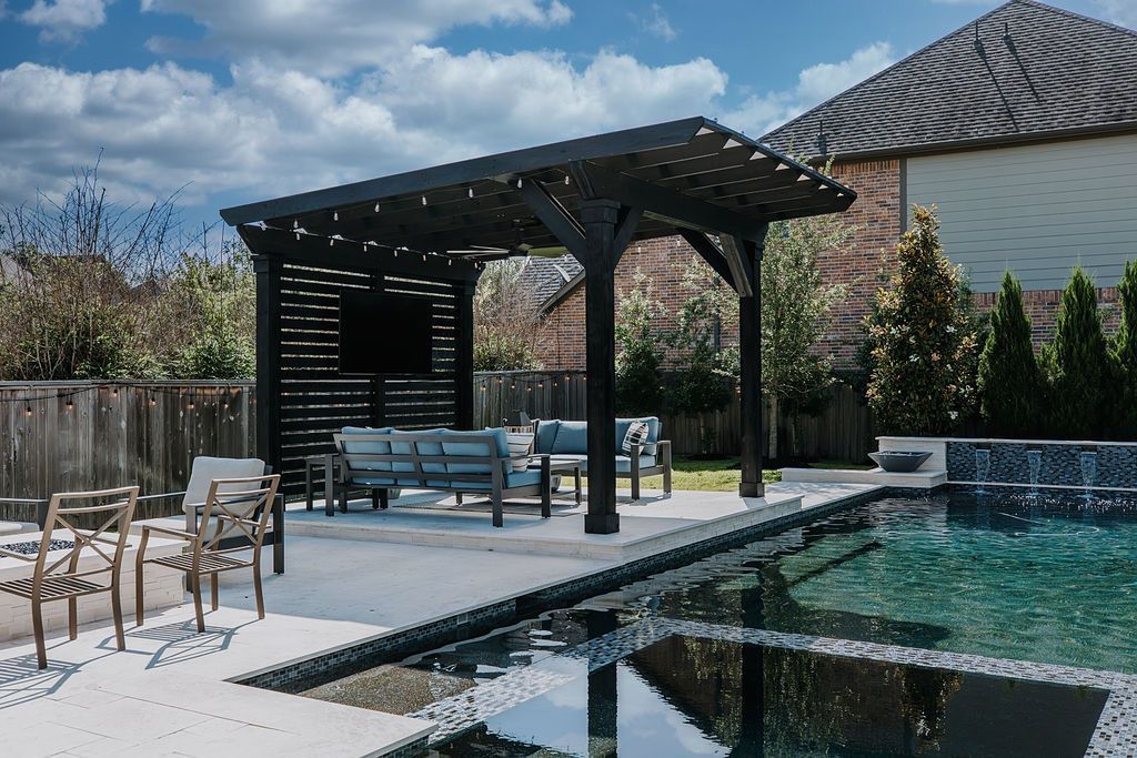 Backyard patio with pergola seating beside a turquoise swimming pool under a bright sky