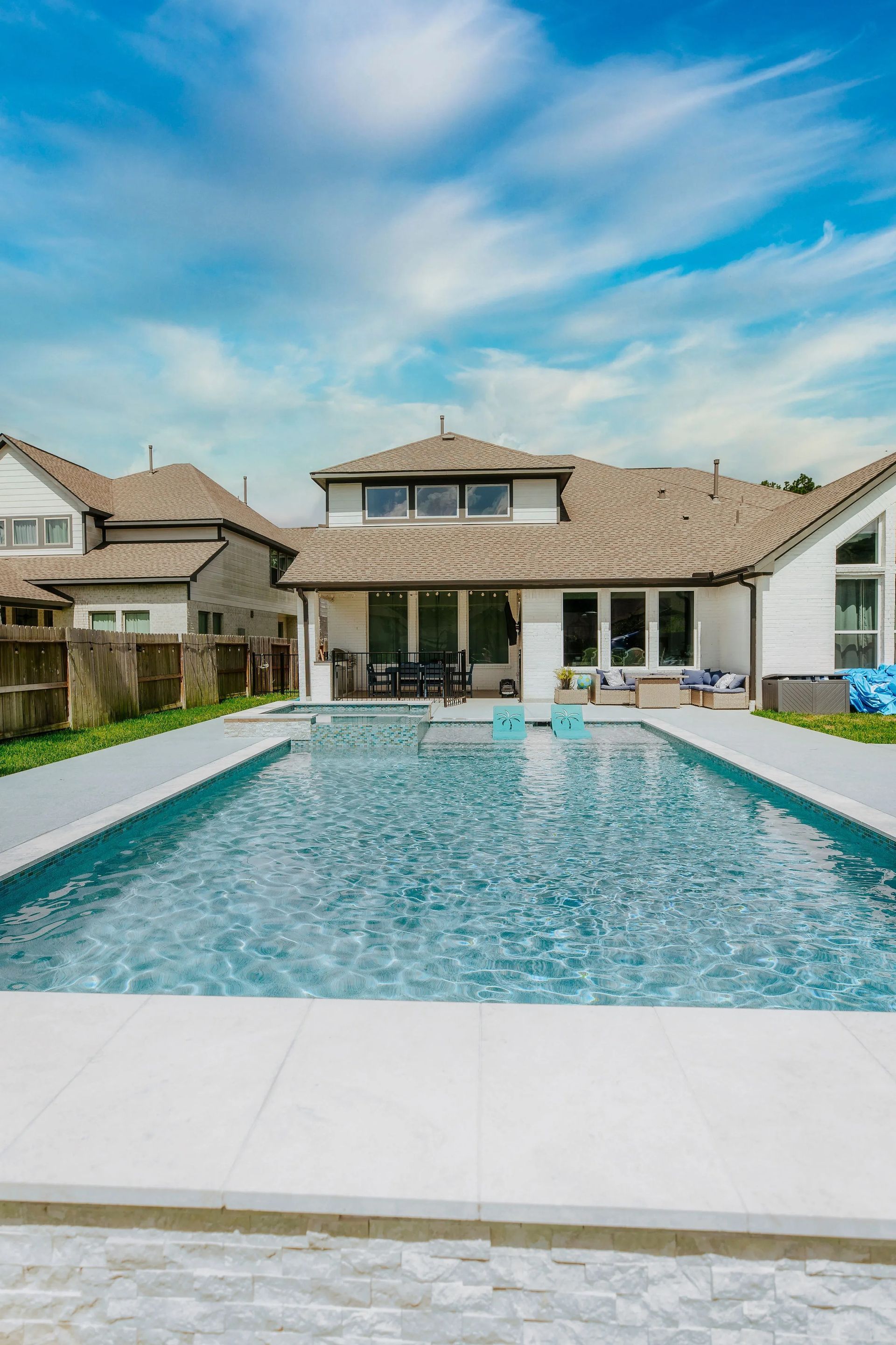 Modern suburban house with a turquoise swimming pool under a blue sky