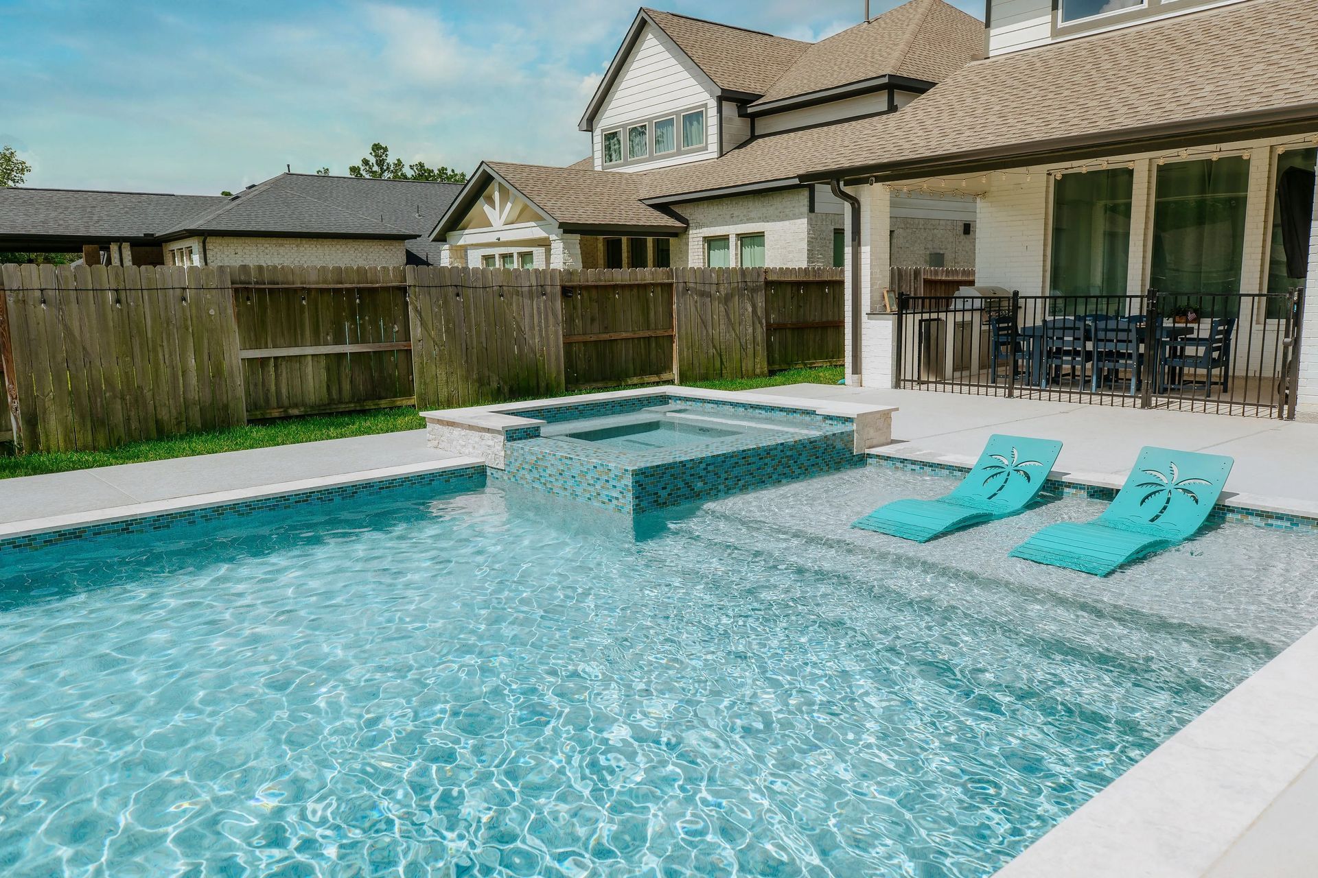 Backyard pool with turquoise water, two loungers, and a covered patio beside a house