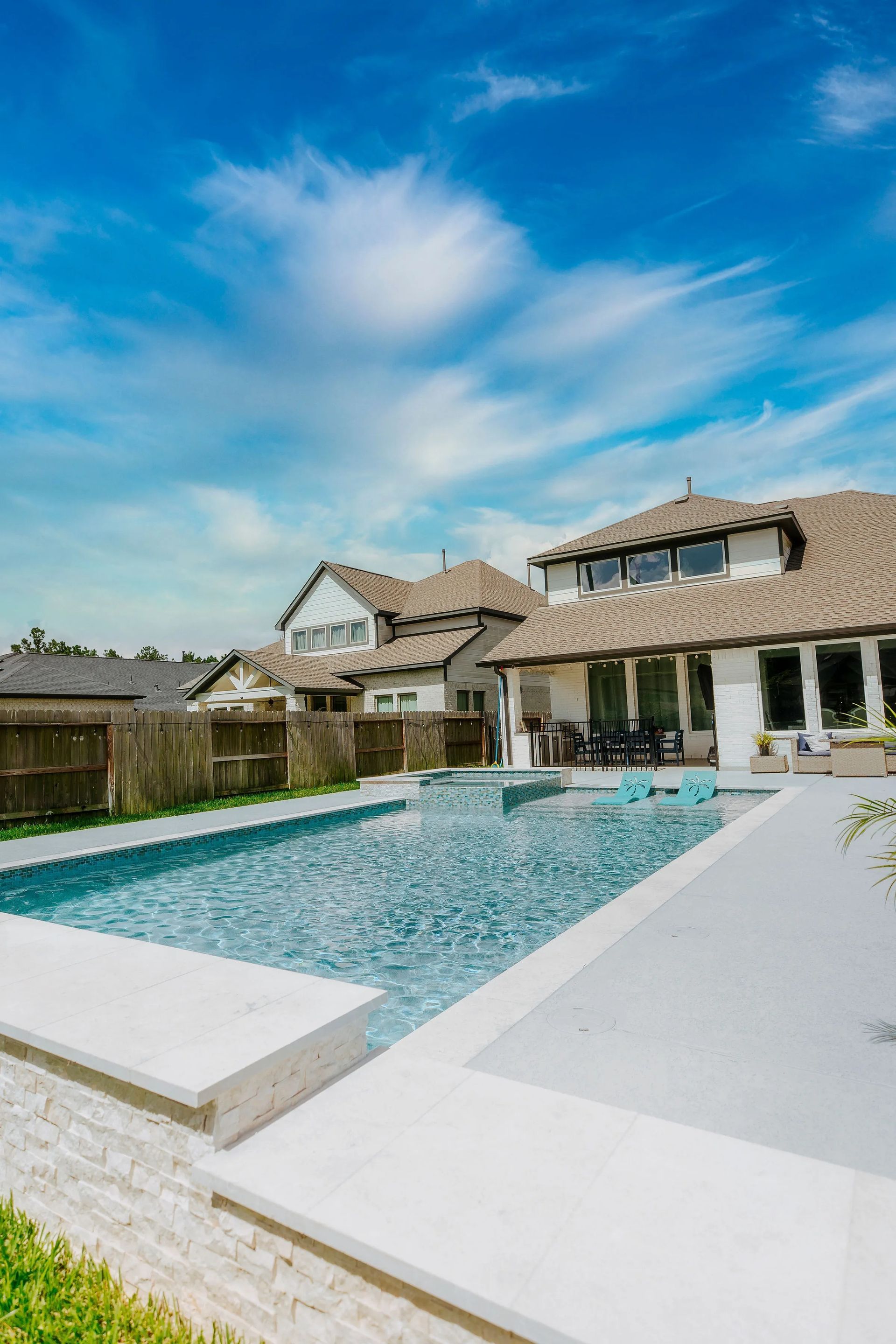 Backyard swimming pool beside a modern house under a bright blue sky