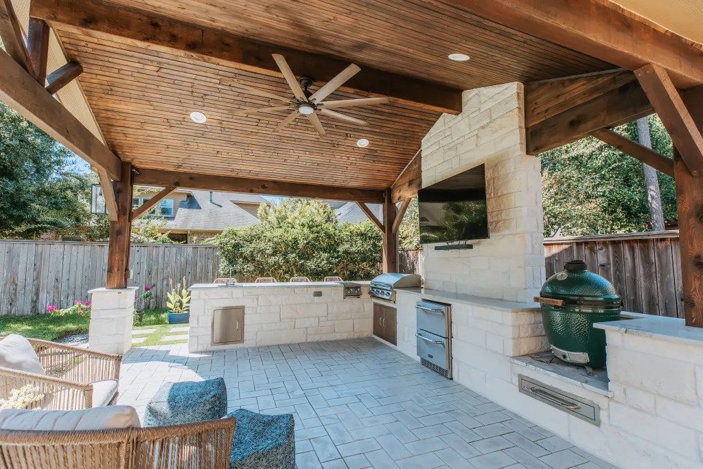 Covered outdoor patio with wicker seating, built-in grill, fan ceiling, and brick fire feature