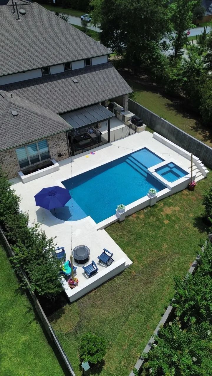 Aerial view of a house backyard with a blue swimming pool, hot tub, patio, and lounge chairs.