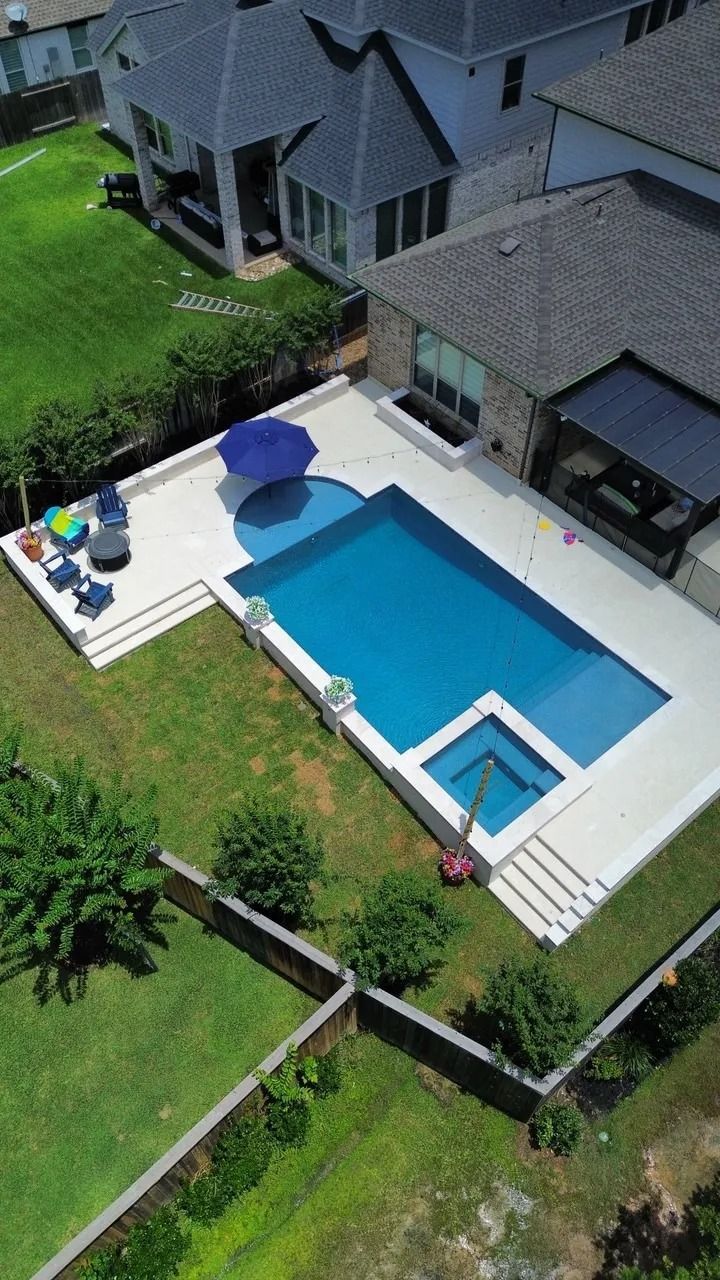 Aerial view of a backyard with a blue swimming pool beside a patio and suburban homes.