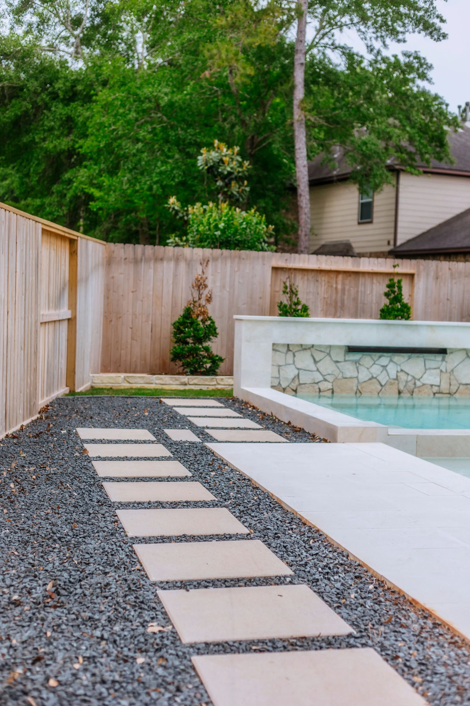 Backyard pool with stepping-stone path, gravel, white deck, and wooden fence