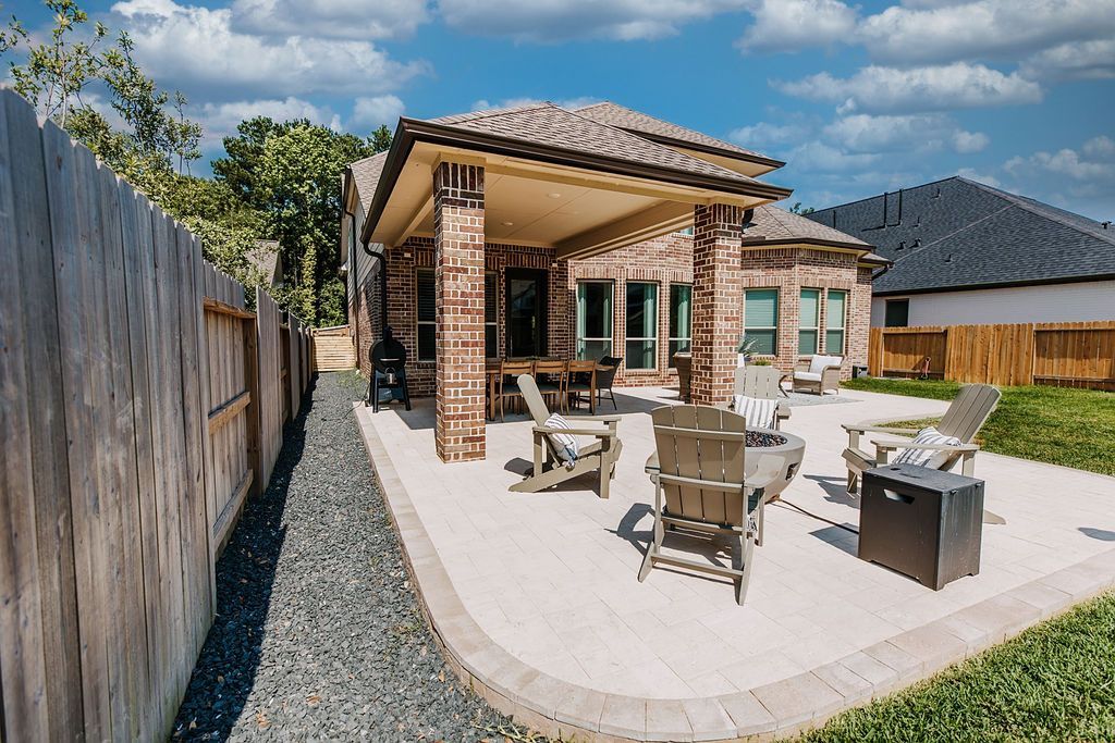Patio with outdoor chairs under a pergola beside a brick house, fenced yard, and gravel landscaping