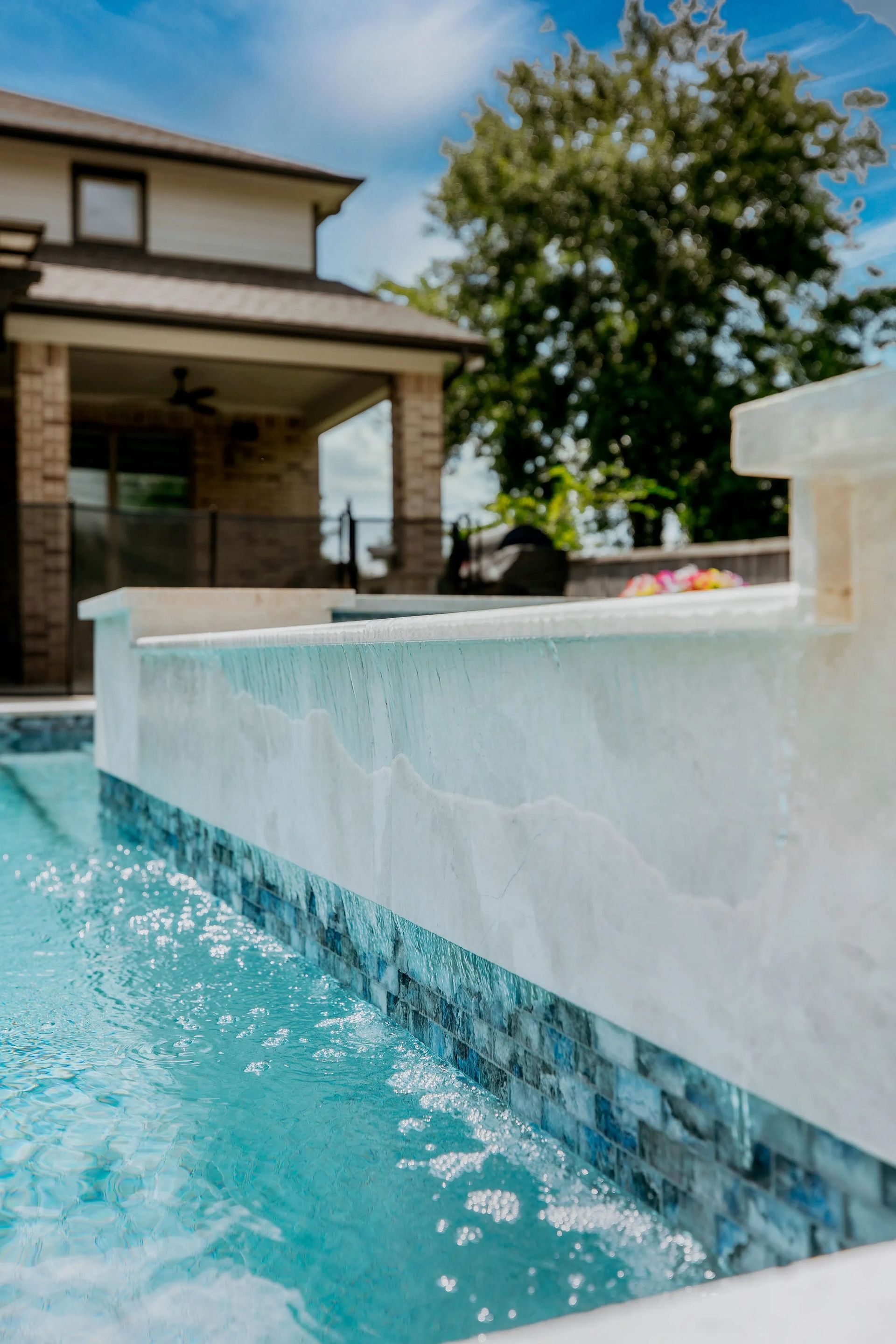 Backyard pool with a white waterfall ledge and turquoise water beside a house