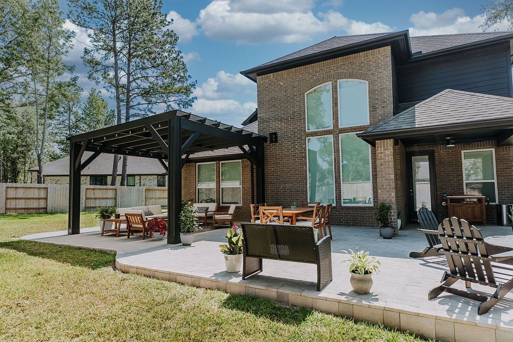 Modern house exterior with covered patio, pergola seating, and grassy yard under a partly cloudy sky