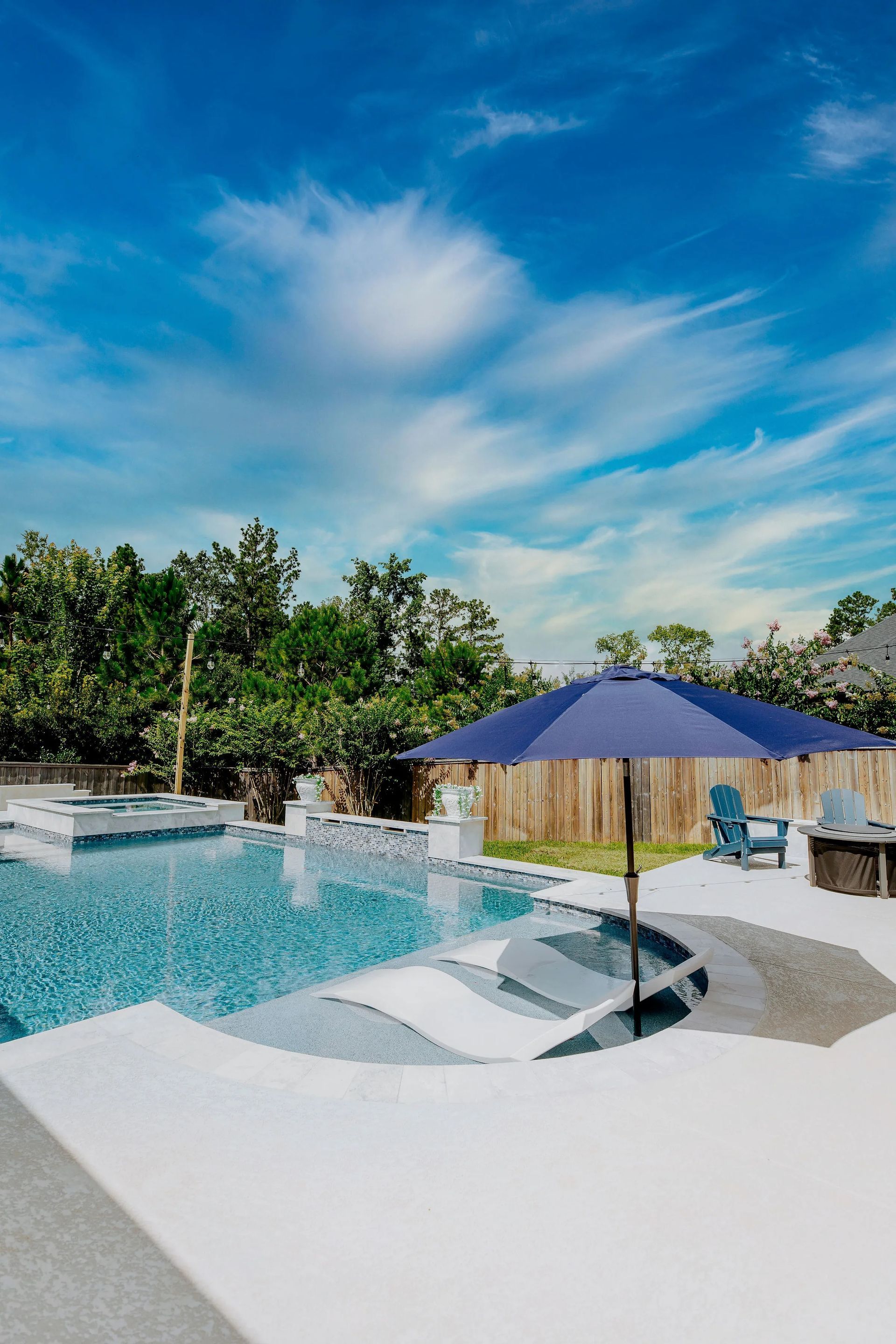 Resort pool with white lounge chairs, blue umbrella, and palm trees under a bright sky