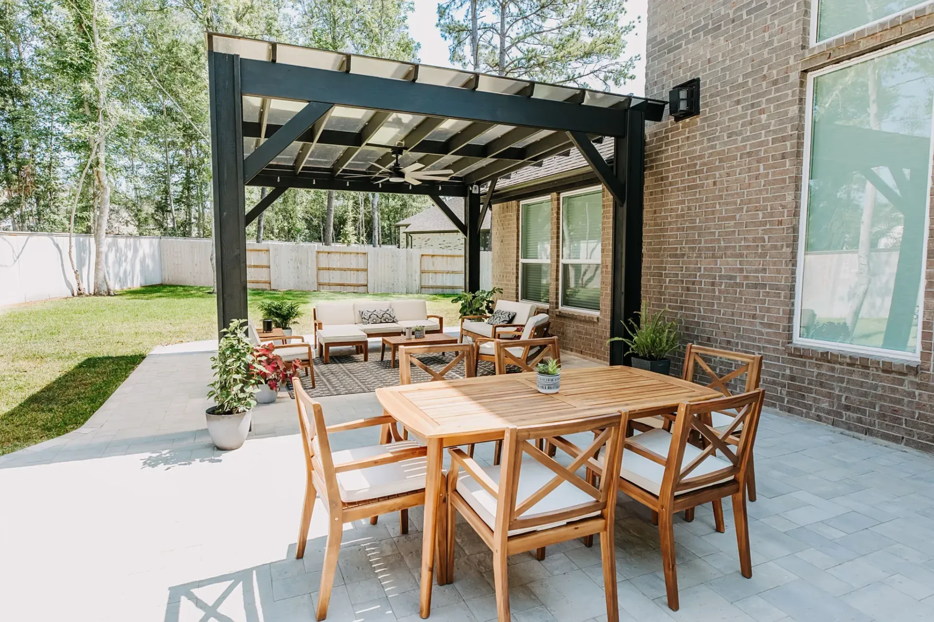 Outdoor patio with wooden dining table and chairs under a black pergola beside a house