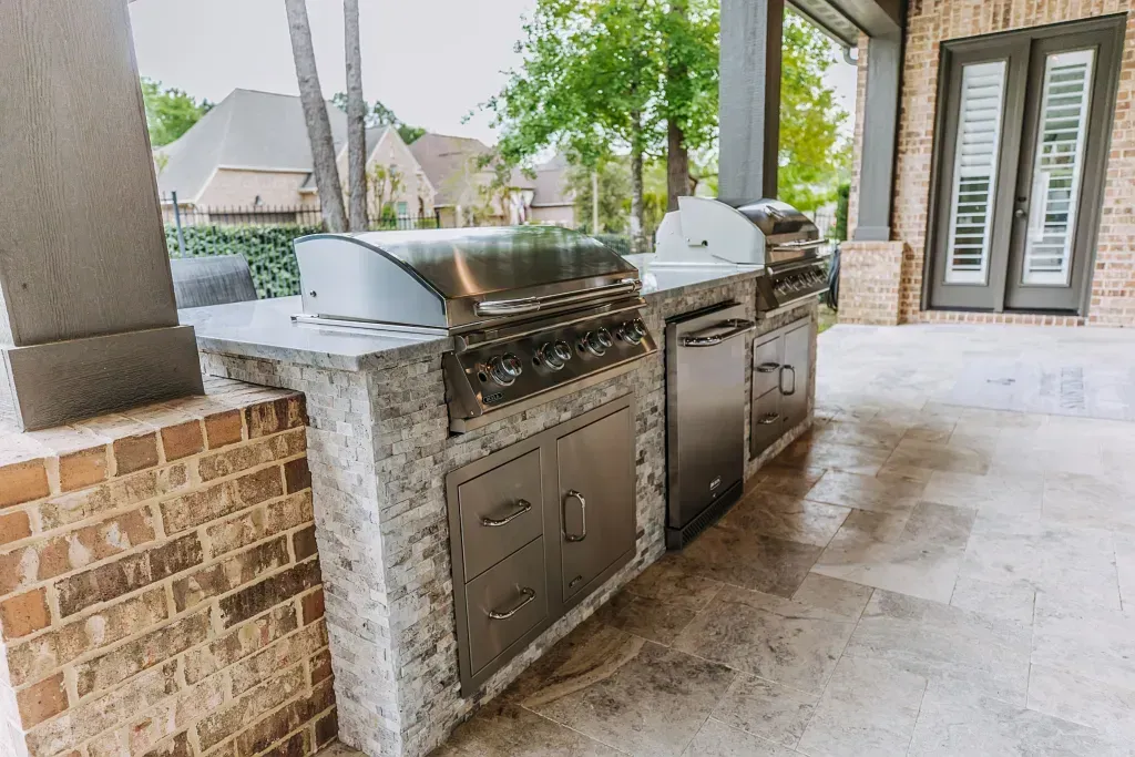 Outdoor stone barbecue grill station with built-in stainless steel grills on a covered patio