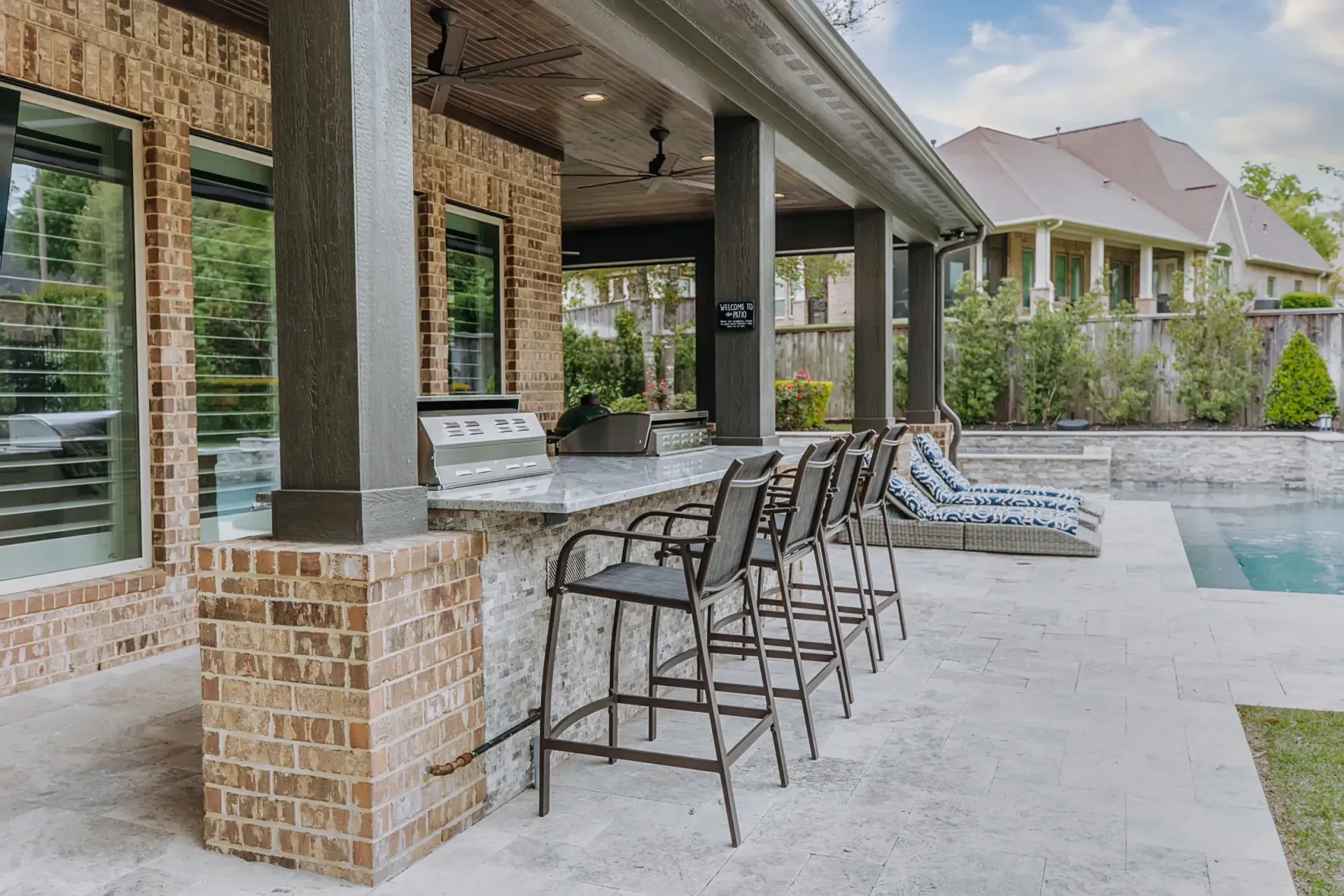 Covered patio with bar stools overlooking a pool in a backyard setting