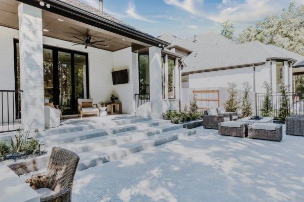 Modern patio with white steps, outdoor seating, and a pergola beside a white house