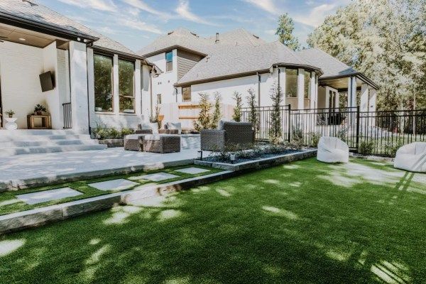 Modern backyard patio with white house, stone steps, and green lawn around a pool area