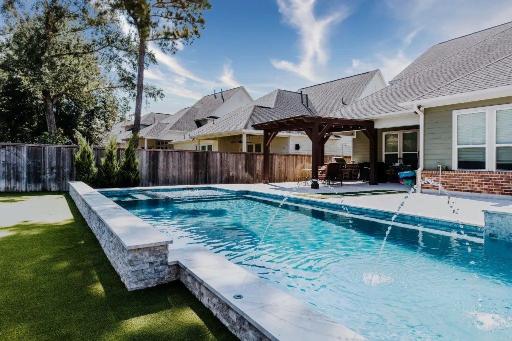 Backyard swimming pool beside a modern house with a covered patio and lawn
