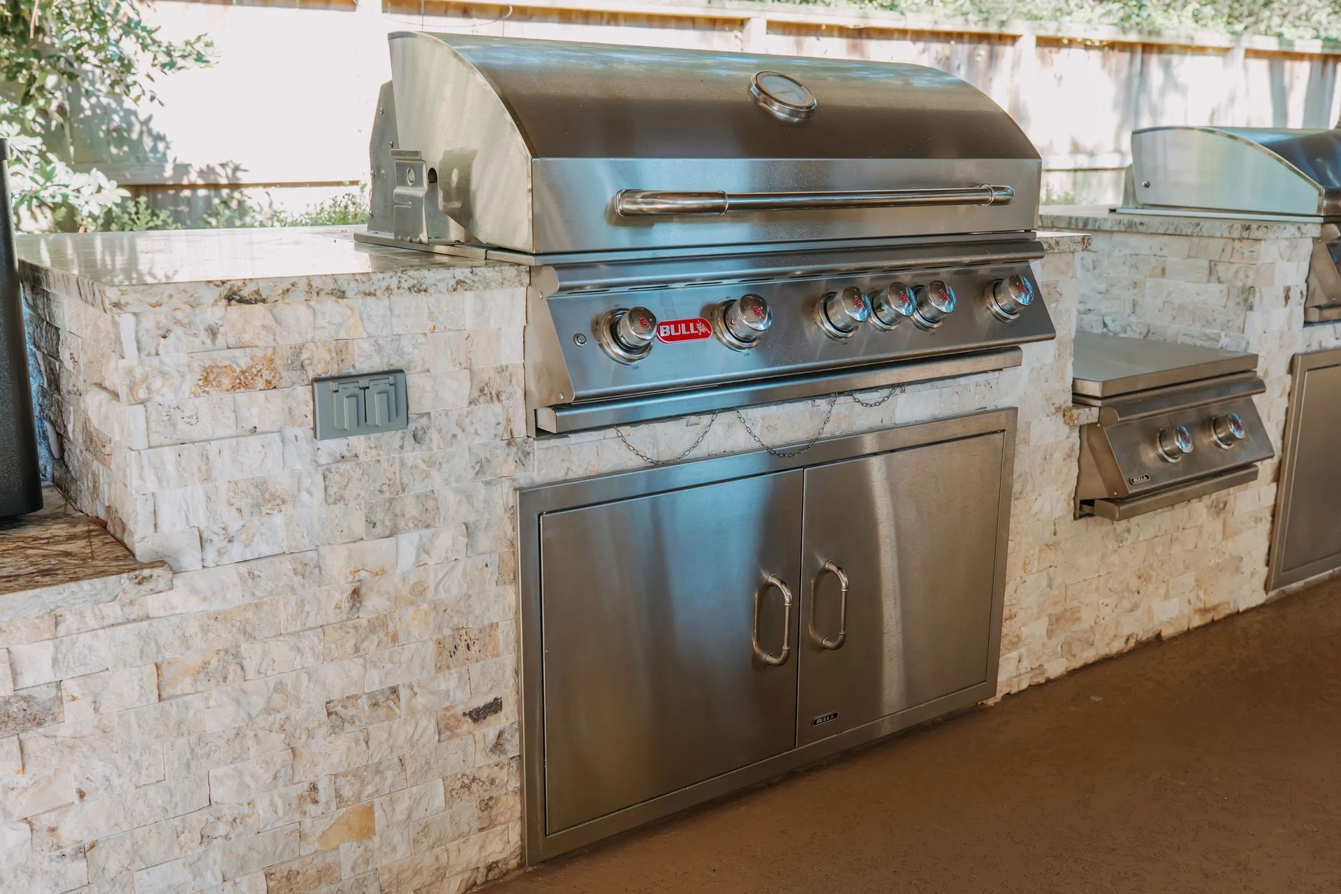 Built-in stainless steel gas grill and side burner on a stone outdoor kitchen counter