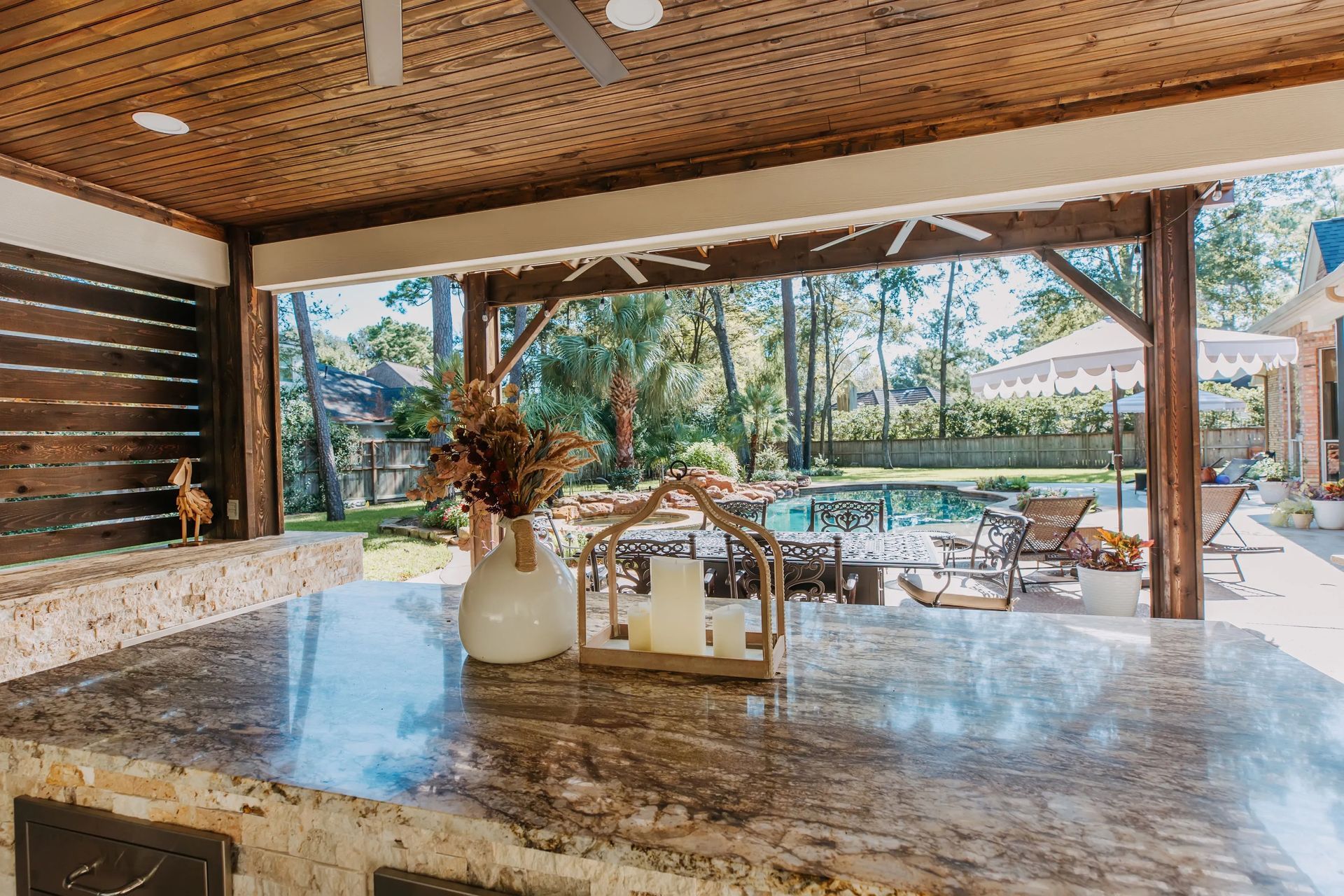 Open-air patio with marble table, wooden ceiling, and tropical garden view beyond a sliding glass wall