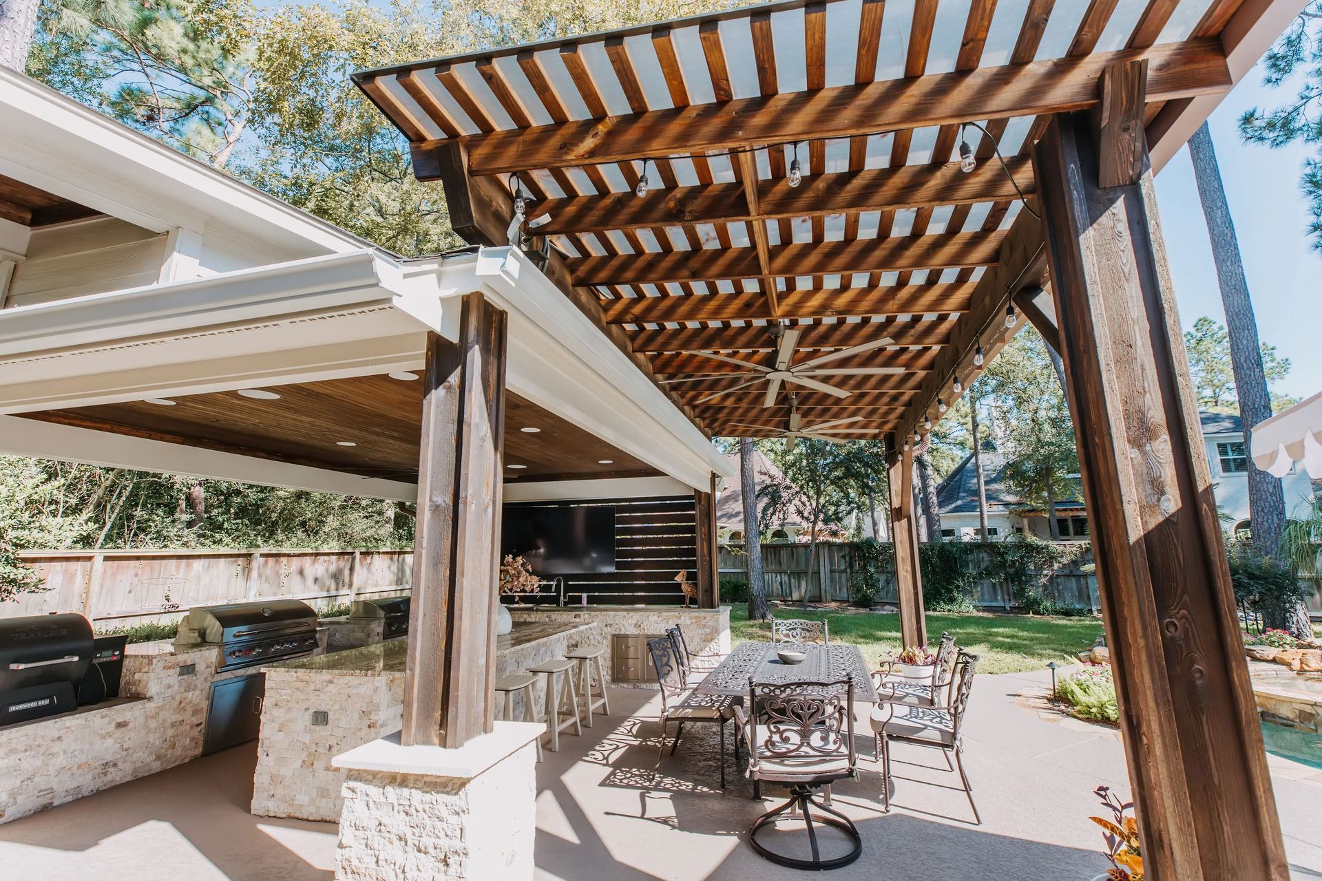 Covered patio with wooden pergola, outdoor dining table, and landscaped backyard in sunlight